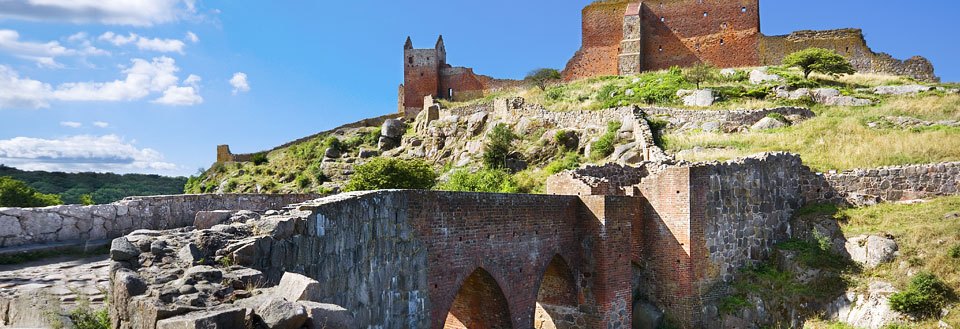 Gamle ruiner af Hammershus-ruinen med brostensbelagte stier og grønne bakker under en blå himmel.