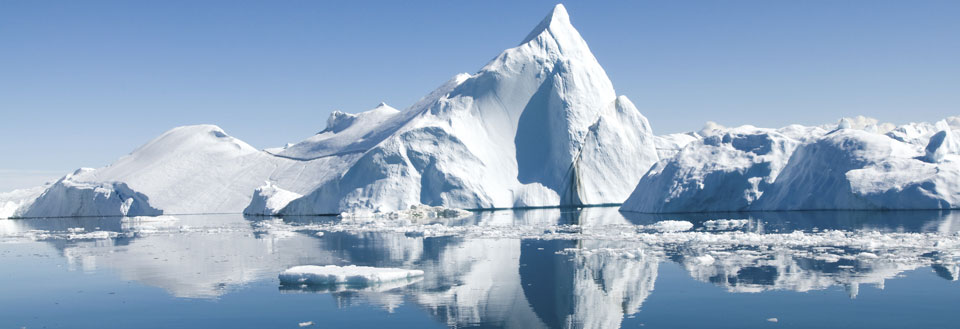 Storslået isbjerg i et roligt polarhav med spejlinger i det krystalklare vand.