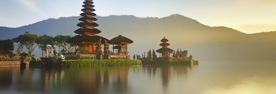 Et fredeligt tempel ved søbred med bjerg i baggrunden ved solopgang.