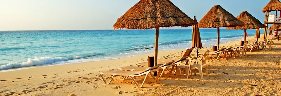 En solrig strand med strandparasoller og liggestole, der står over for det rolige turkisblå hav.