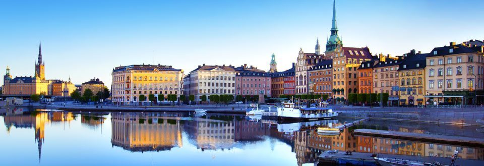 Stockholm ved tusmørke, med spejlinger af farverige bygninger og både.