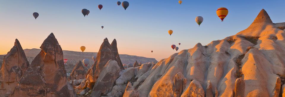 Farverige varmluftballoner, der svæver over et unikt klippelandskab ved solnedgang.