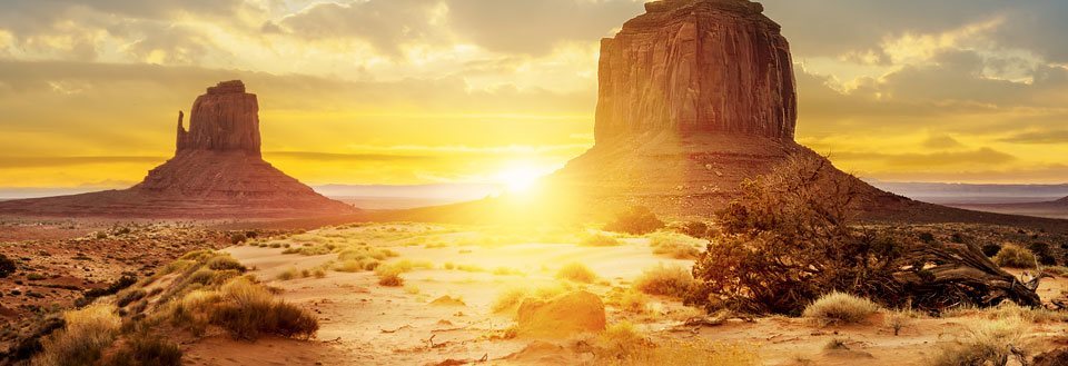 En ørken ved solnedgang med markante klippeformationer og et gyldent lys.
