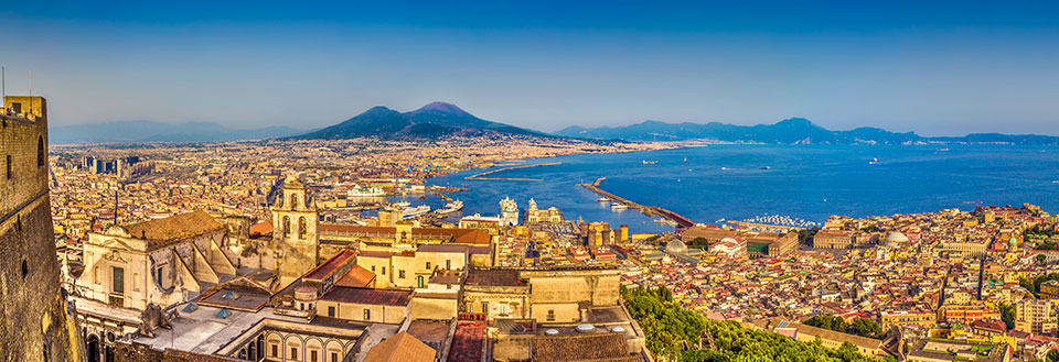 Panoramaudsigt over en livlig by med historiske bygninger og en berømt vulkan i baggrunden.