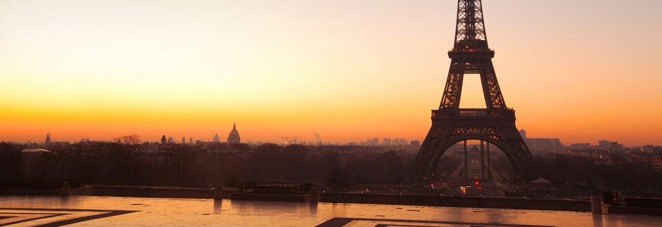 Solnedgang bag Eiffeltårnet i Paris med en varm orange himmel og silhuetten af byens skyline.