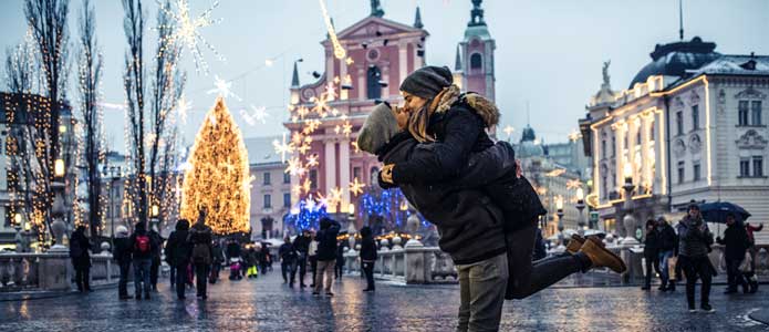 Par kysser hinanden på gade med stort juletræ og smukkebygninger