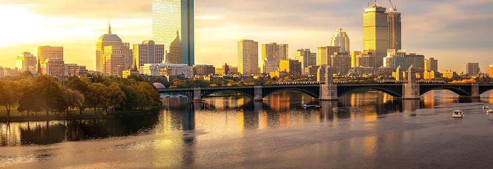 Billedet viser en skyline af Boston ved solnedgang med højhuse, en bro, og refleksioner i vand.