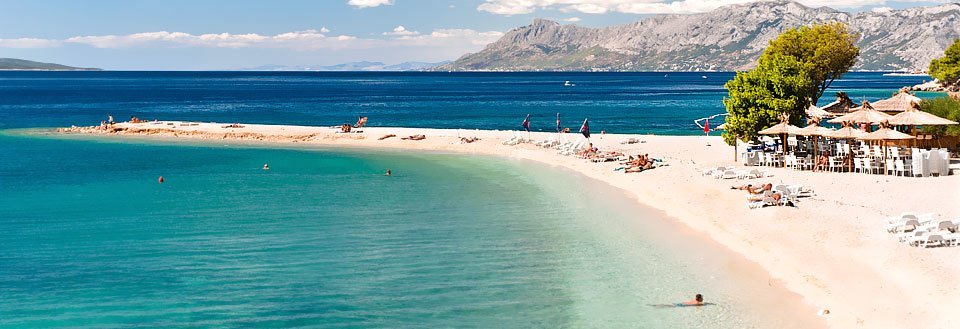 Et idyllisk strandbillede med krystalklart vand, hvide sandstrande og bjerglandskab i baggrunden.