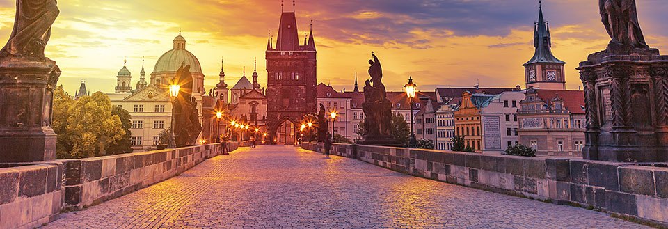 Solnedgang over en Karlsbroen i Prag  med historiske tårne og statuer, en malerisk bysilhuet i baggrunden.