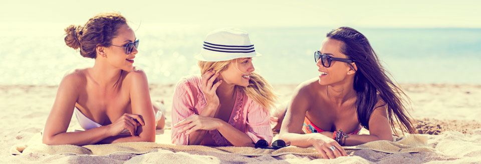 Tre veninder nyder solen og samværet på en sandstrand i Sunny Beach, mens de ligger på et tæppe.