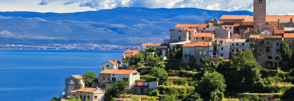 Billedet viser en idyllisk kystby med farverige huse og en klar blå himmel. Havet spejler byens skønhed.