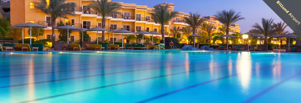 Et luksuriøst resort med swimmingpool i skumringen. Liggestole og parasoller står ved poolkanten. Et luksuriøst resort med swimmingpool i skumringen. Liggestole og parasoller står ved poolkanten.