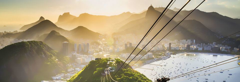 Billede af en svævebane med udsigt over Rio de Janeiro omringet af bakker og vand ved solnedgang.