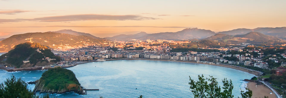 San Sebastian ved solnedgang med bjerge i baggrunden og en buet strand foran.