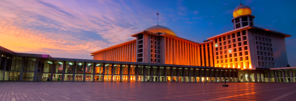 Stor bygning med kupler, oplyst ved skumring. Himlen er farverig med nuancer af blå og orange.