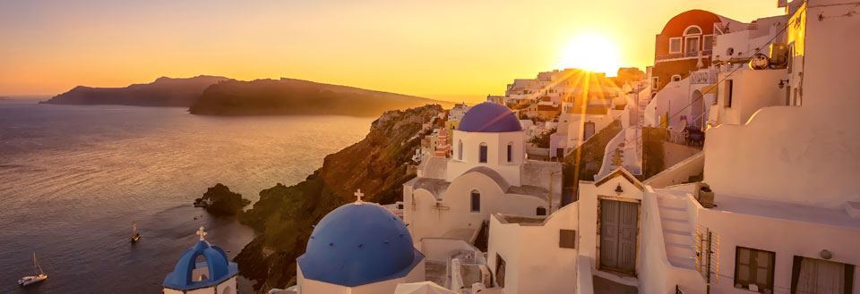 Solnedgang over hvide bygninger med blå kupler ved havet på Santorini. En malerisk græsk øudsigt.