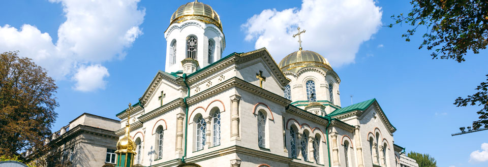 En majestætisk kirke med gyldne kupler og hvid facade mod en blå himmel med få skyer.