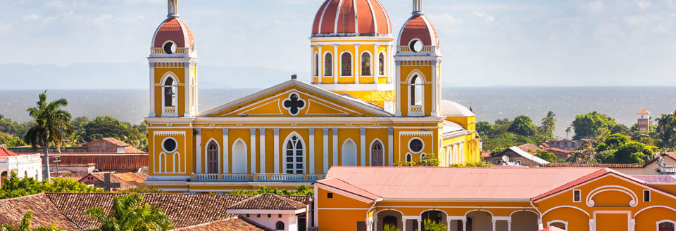 Farverig katedral med to tårne og kupler, omgivet af klassiske bygninger mod blå himmel.