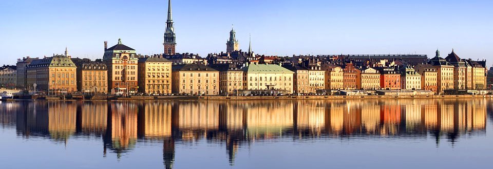 Panoramaudsigt over Stockholm bygninger spejlet i vandet ved solnedgang.