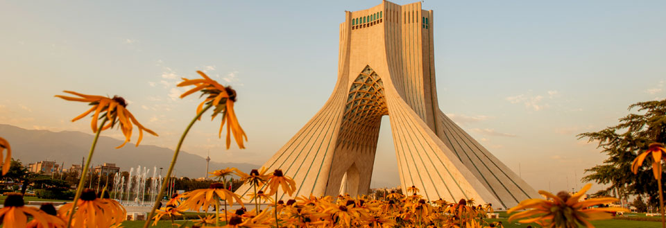 Ikonisk betonkonstruktion med karakteristisk arkitektur, omgivet af blomster og springvand i solnedgang.