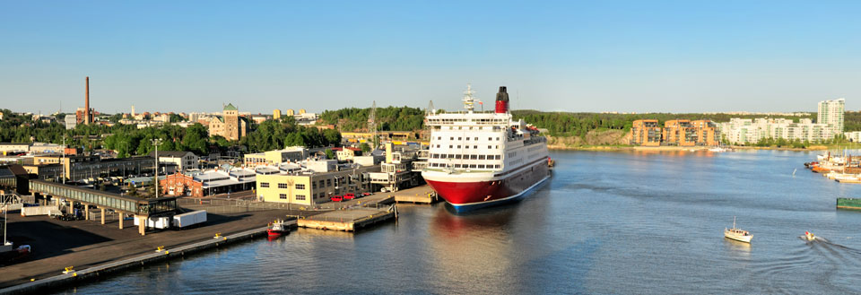 Havnefront med bygninger, et stort passagerskib og mindre både på en solrig dag.