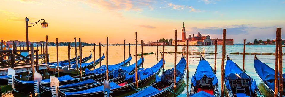 Solnedgang i Venedig med gondoler forankret ved træpæle, og San Giorgio Maggiore kirken i baggrunden.