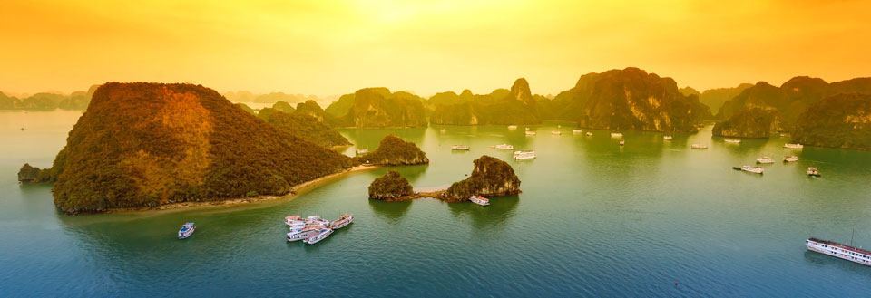 Dramatisk solnedgangslys over Halong Bay med kalkstensøer og sejlbåde.