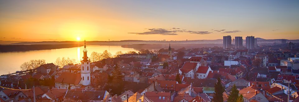 By ved solnedgang med silhuetten af en kirke og moderne bygninger i baggrunden.