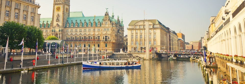 Panoramaudsigt over en kanal i en by med bygninger, en båd og flag.